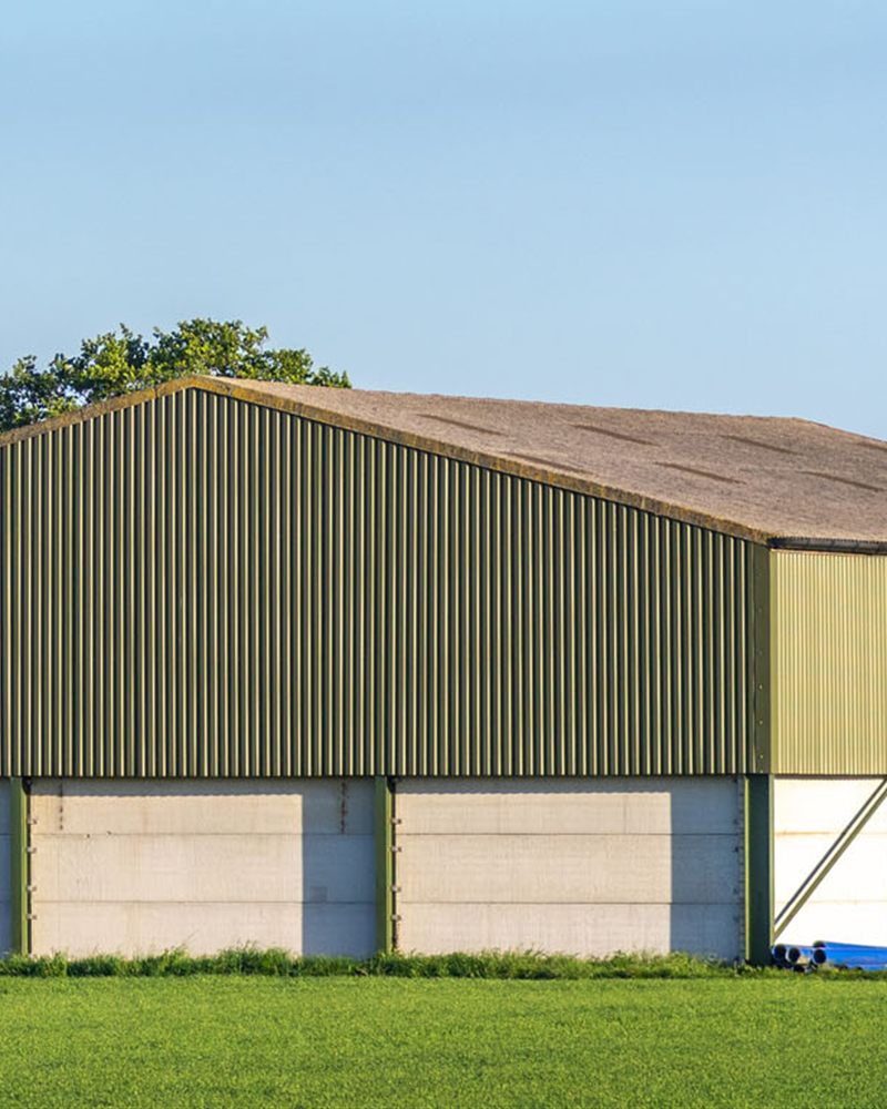 A green steel-frame agricultural barn in a farm field