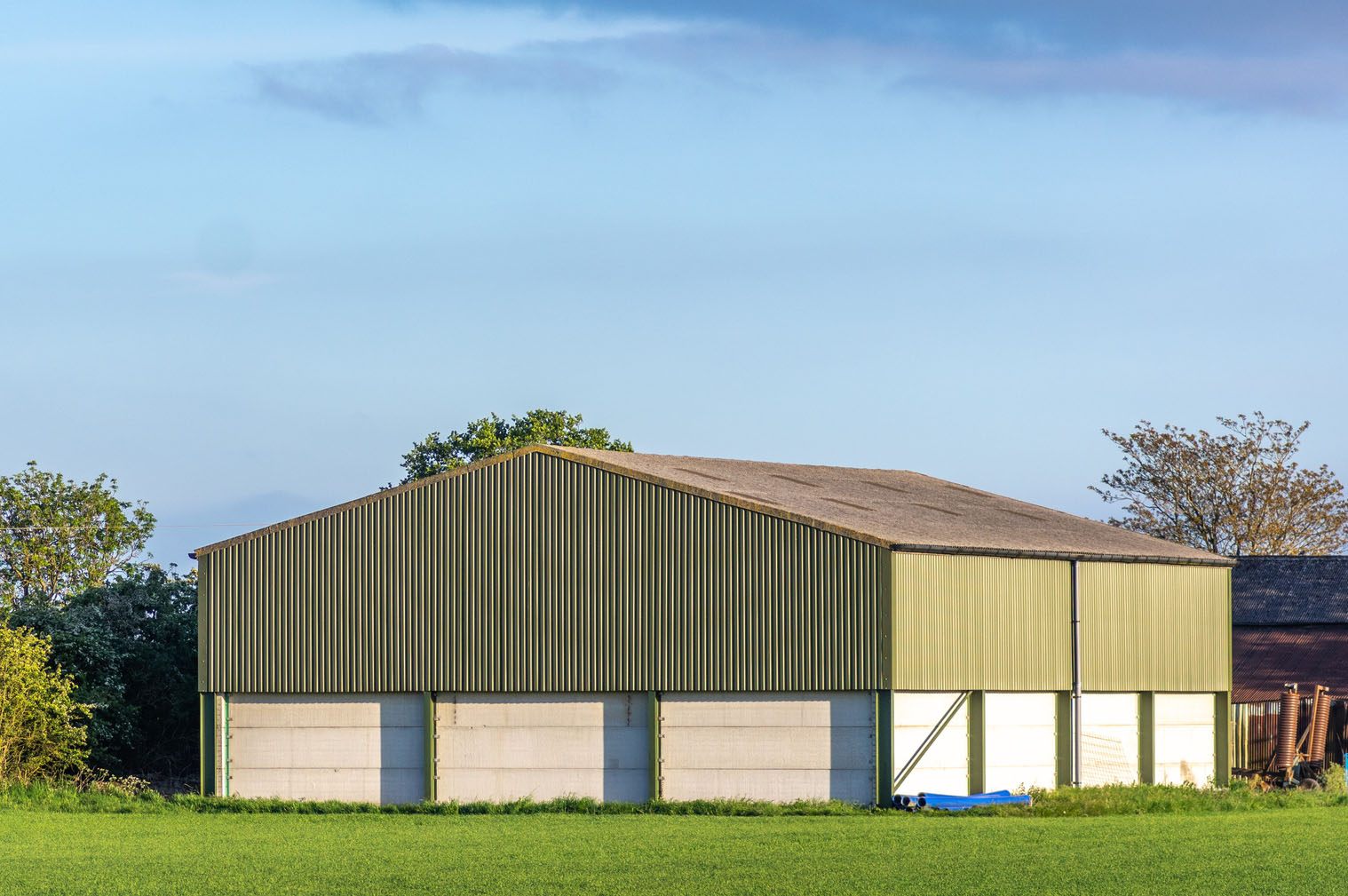 A green steel-frame agricultural barn in a farm field